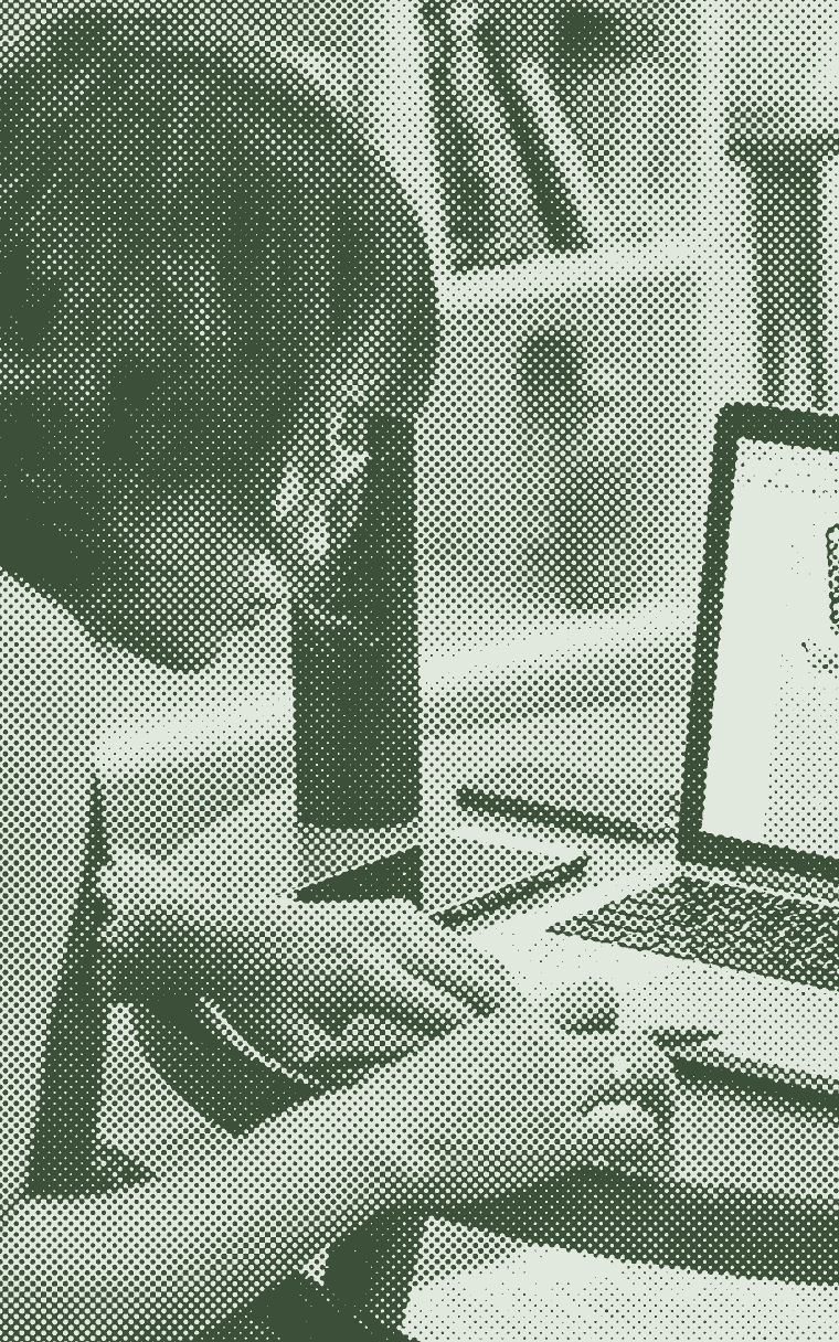 Someone taking notes at a home desk beside an open laptop
