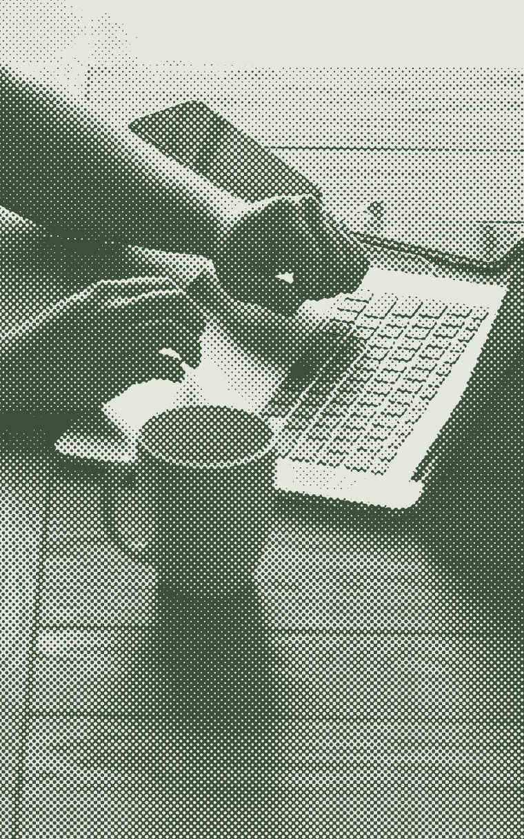 Hands typing on a laptop at a dark table, a mug beside it